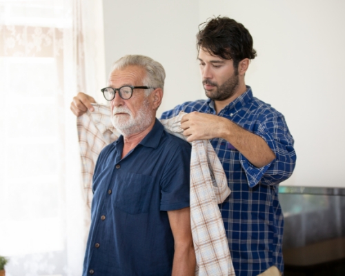 Caregiver helping man put on shirt