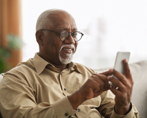 Older Black man smiling while on phone. 